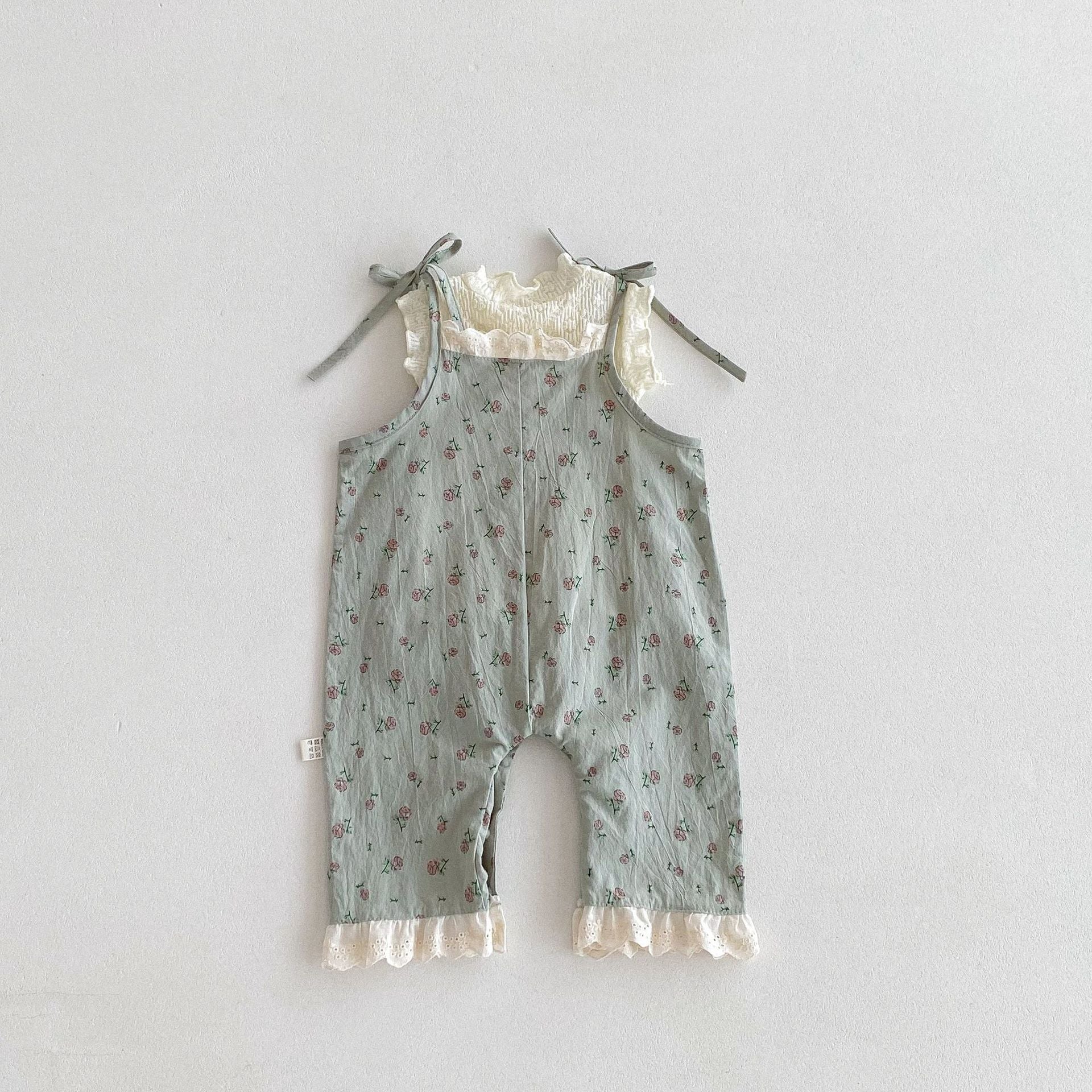 A cute baby girl wearing a green sleeveless floral pattern strap romper, perfect for summer outings.