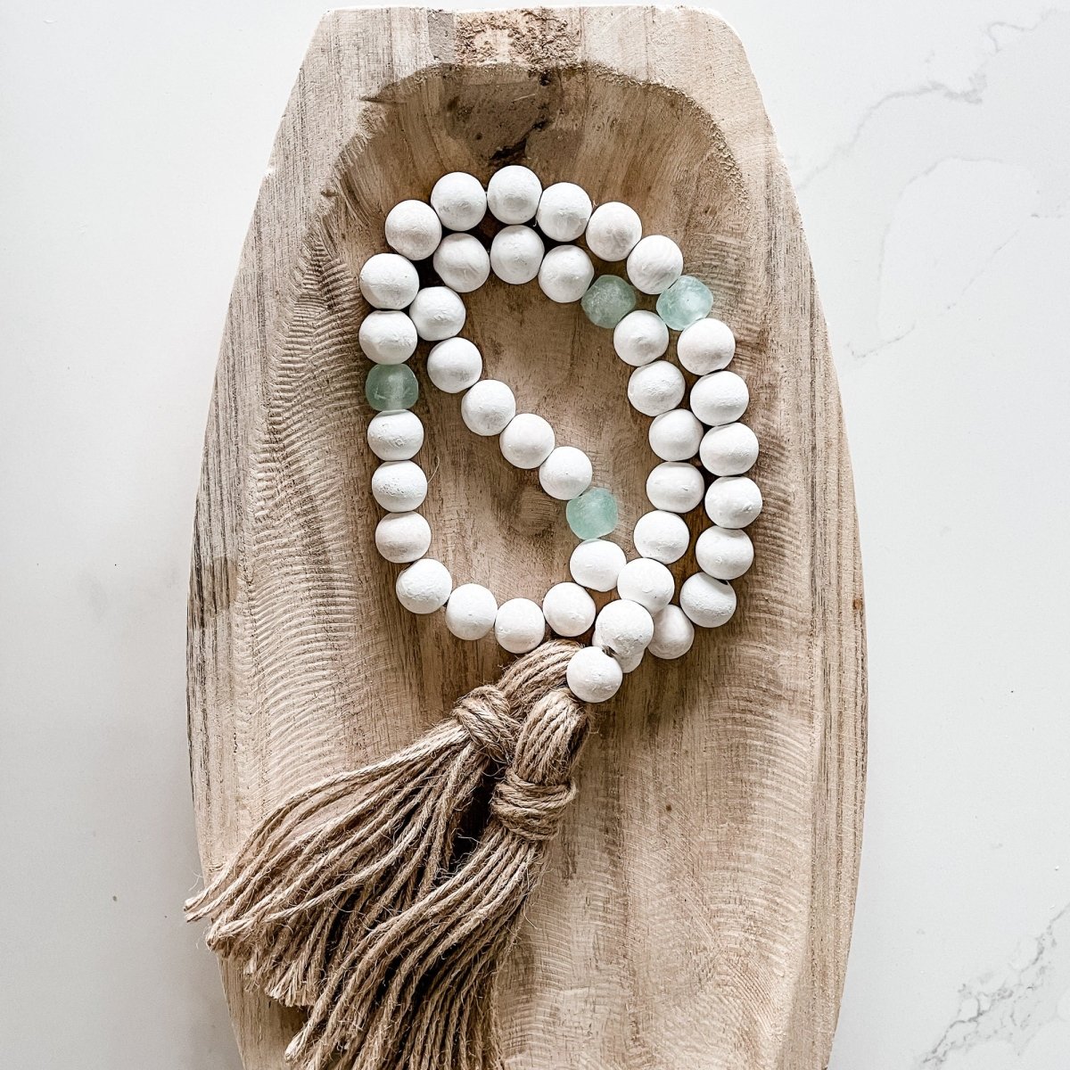 A beautiful whitewashed wood bead garland featuring jumbo aqua recycled glass beads and jute tassels, perfect for coastal decor.