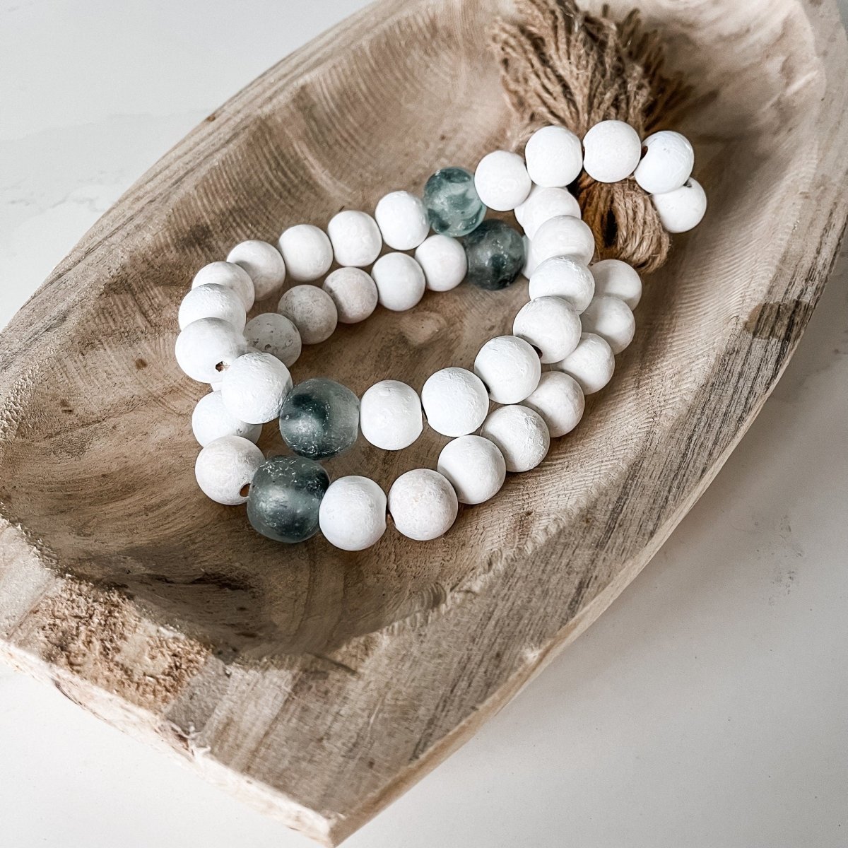 A beautiful whitewashed wood bead garland featuring jumbo gray recycled glass beads and jute tassels, perfect for coastal decor.