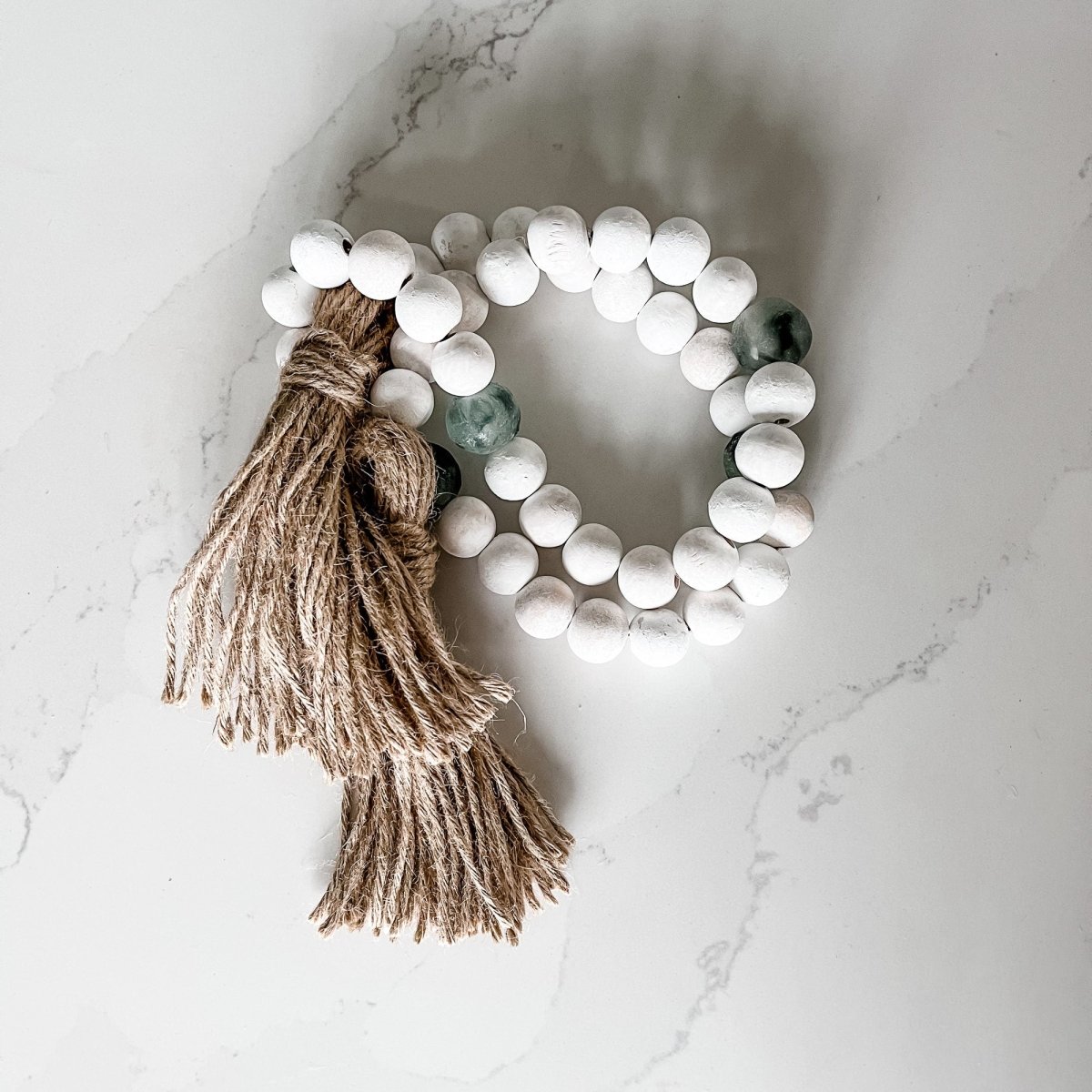 A beautiful whitewashed wood bead garland featuring jumbo gray recycled glass beads and jute tassels, perfect for coastal decor.