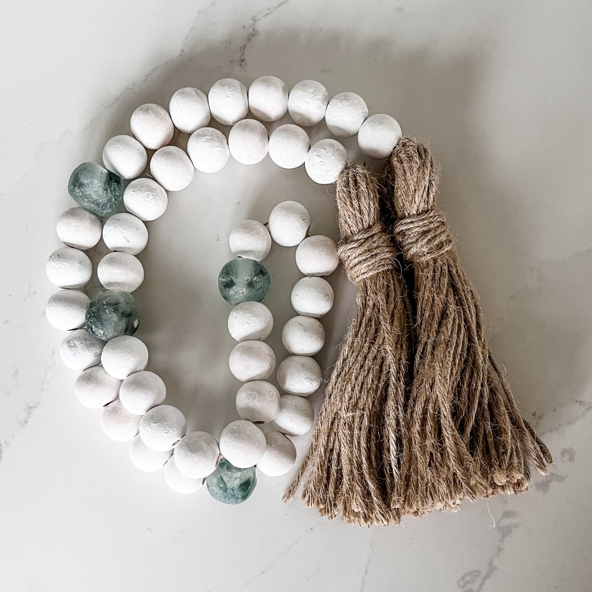 A beautiful whitewashed wood bead garland featuring jumbo gray recycled glass beads and jute tassels, perfect for coastal decor.