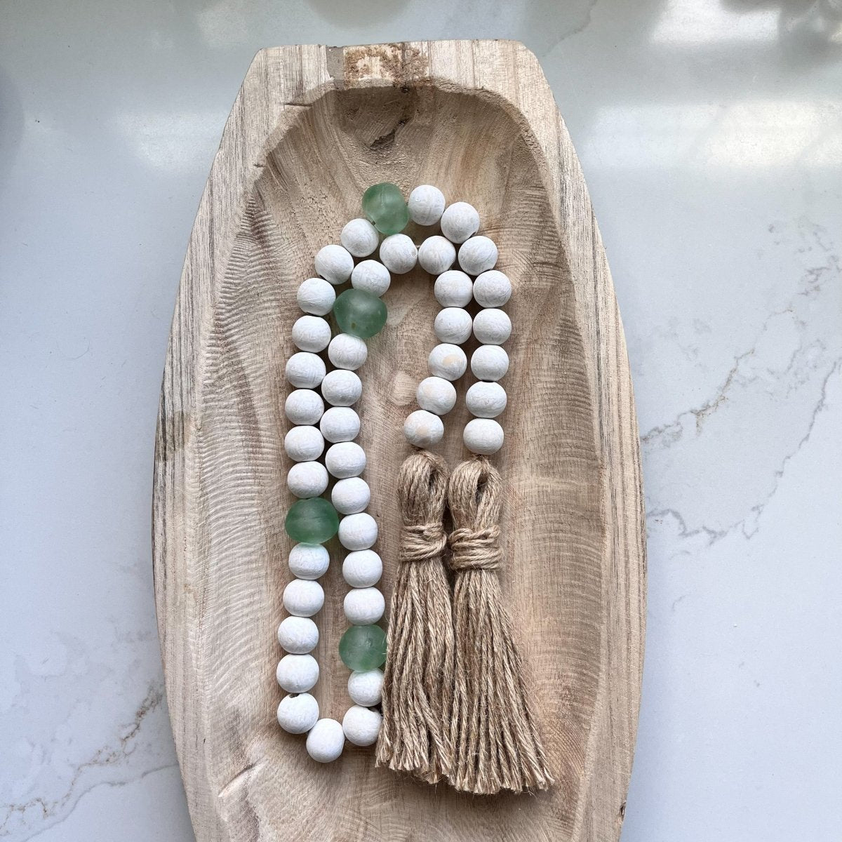 A beautifully handcrafted whitewashed wood bead garland featuring jumbo green and aqua recycled glass beads, adorned with jute tassels.