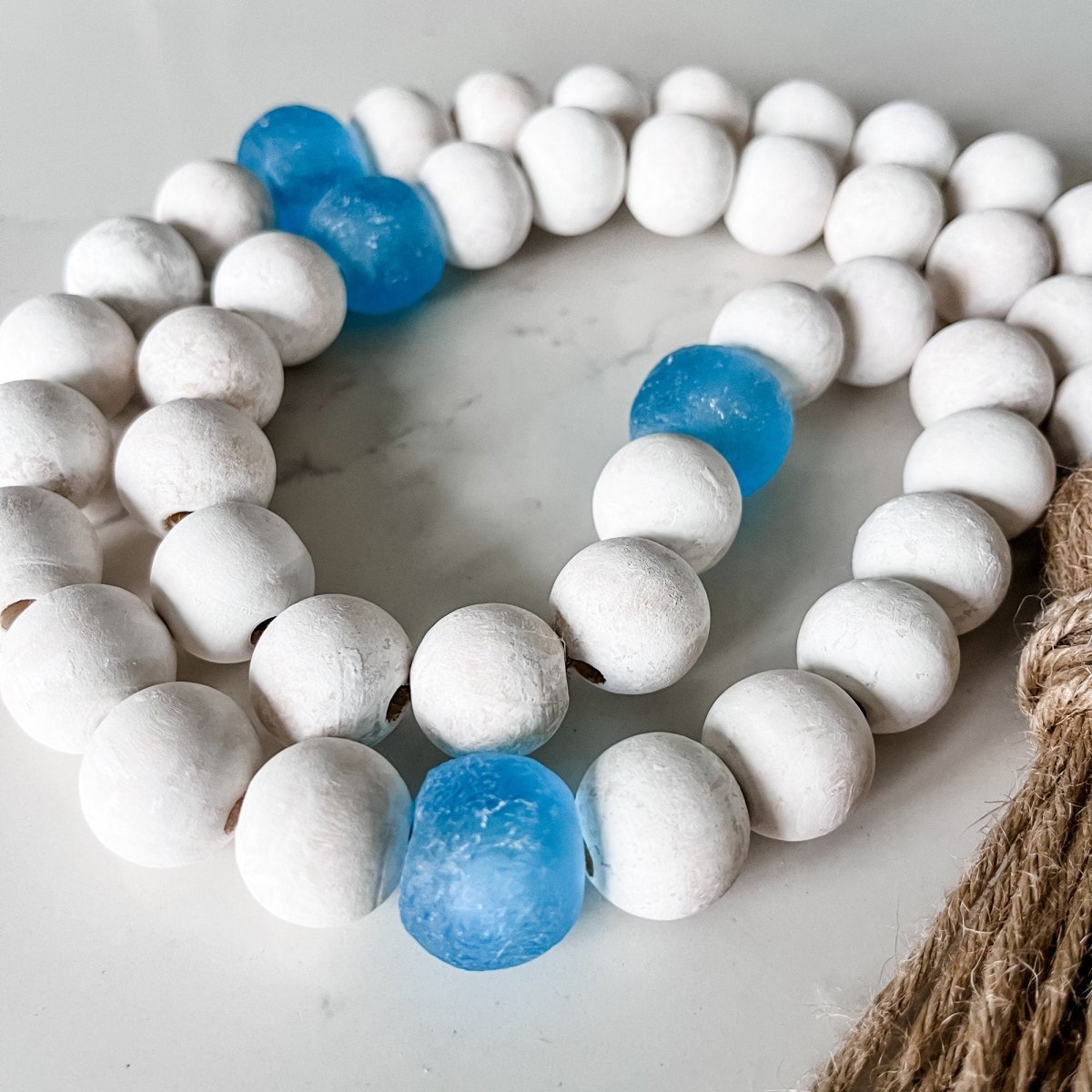 A beautiful Whitewashed Wood Bead Garland featuring Jumbo Ice Blue Recycled Glass Beads, perfect for coastal decor.