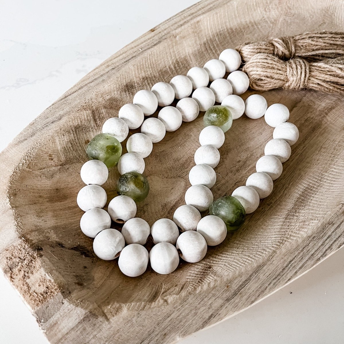 A beautifully crafted Whitewashed Wood Bead Garland featuring Jumbo Olive Green Recycled Glass beads and jute tassels, perfect for coastal decor.