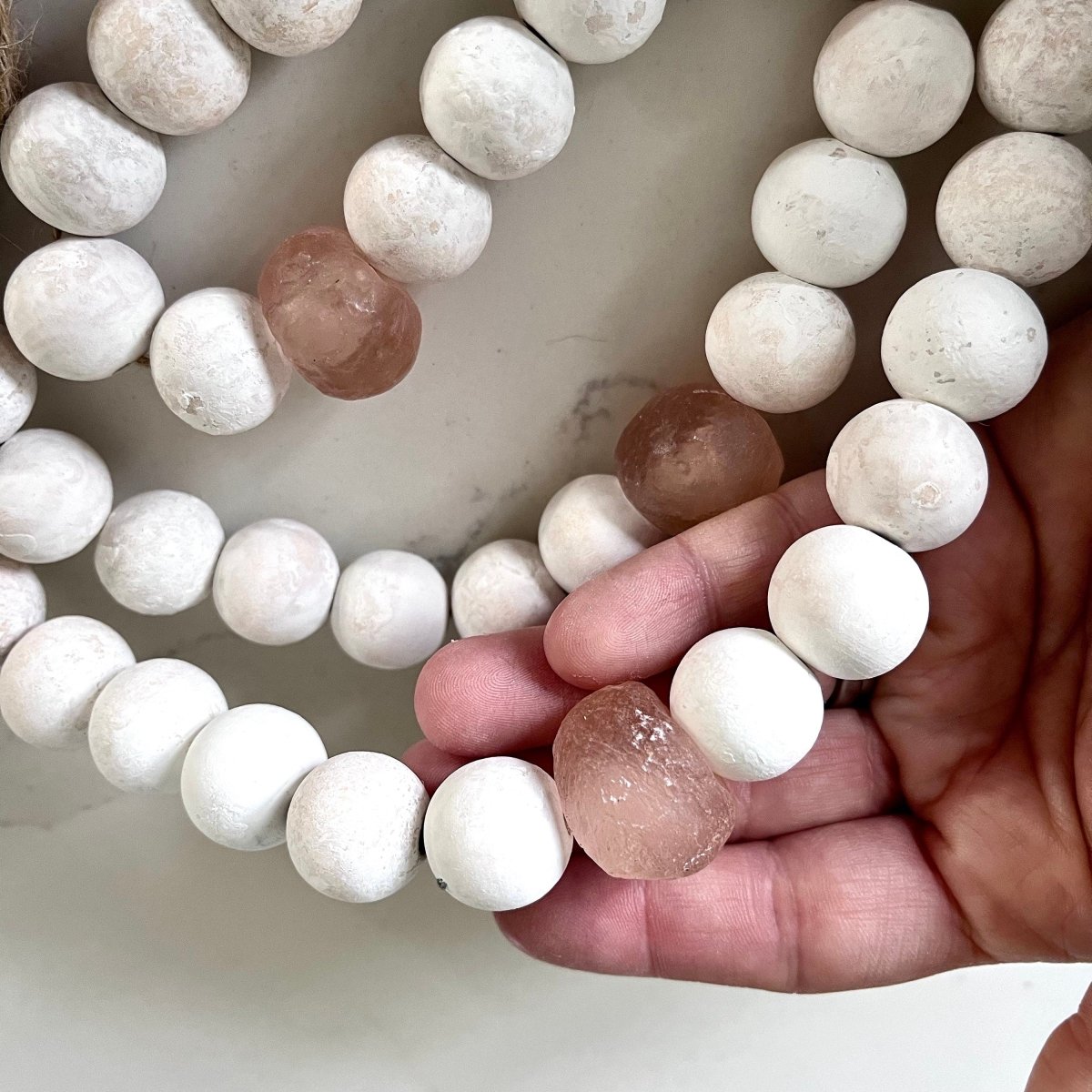 A beautiful whitewashed wood bead garland featuring jumbo rose recycled glass beads and jute tassels, perfect for coastal decor.