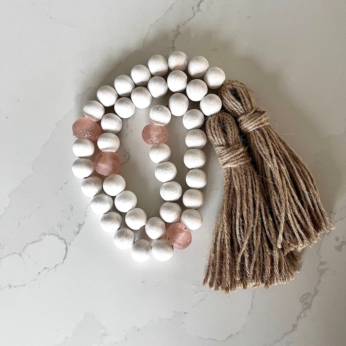 A beautiful whitewashed wood bead garland featuring jumbo rose recycled glass beads and jute tassels, perfect for coastal decor.