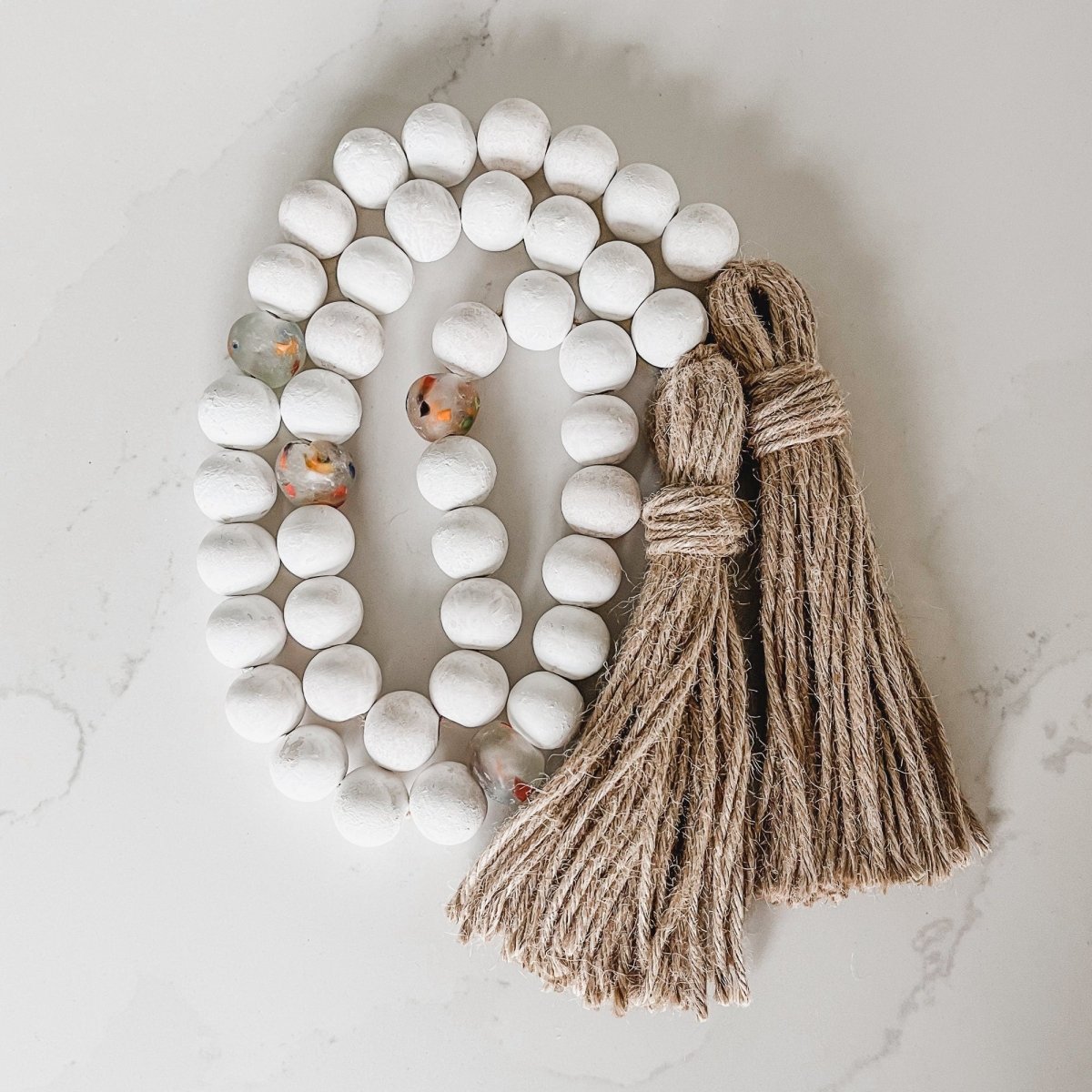 A beautiful Whitewashed Wood Bead Garland featuring multi-colored recycled glass beads and jute tassels, perfect for coastal decor.