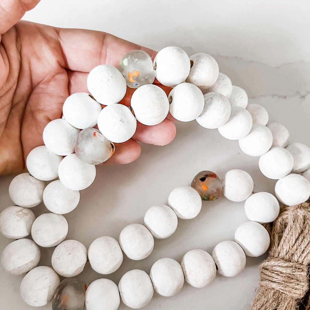 A beautiful Whitewashed Wood Bead Garland featuring multi-colored recycled glass beads and jute tassels, perfect for coastal decor.