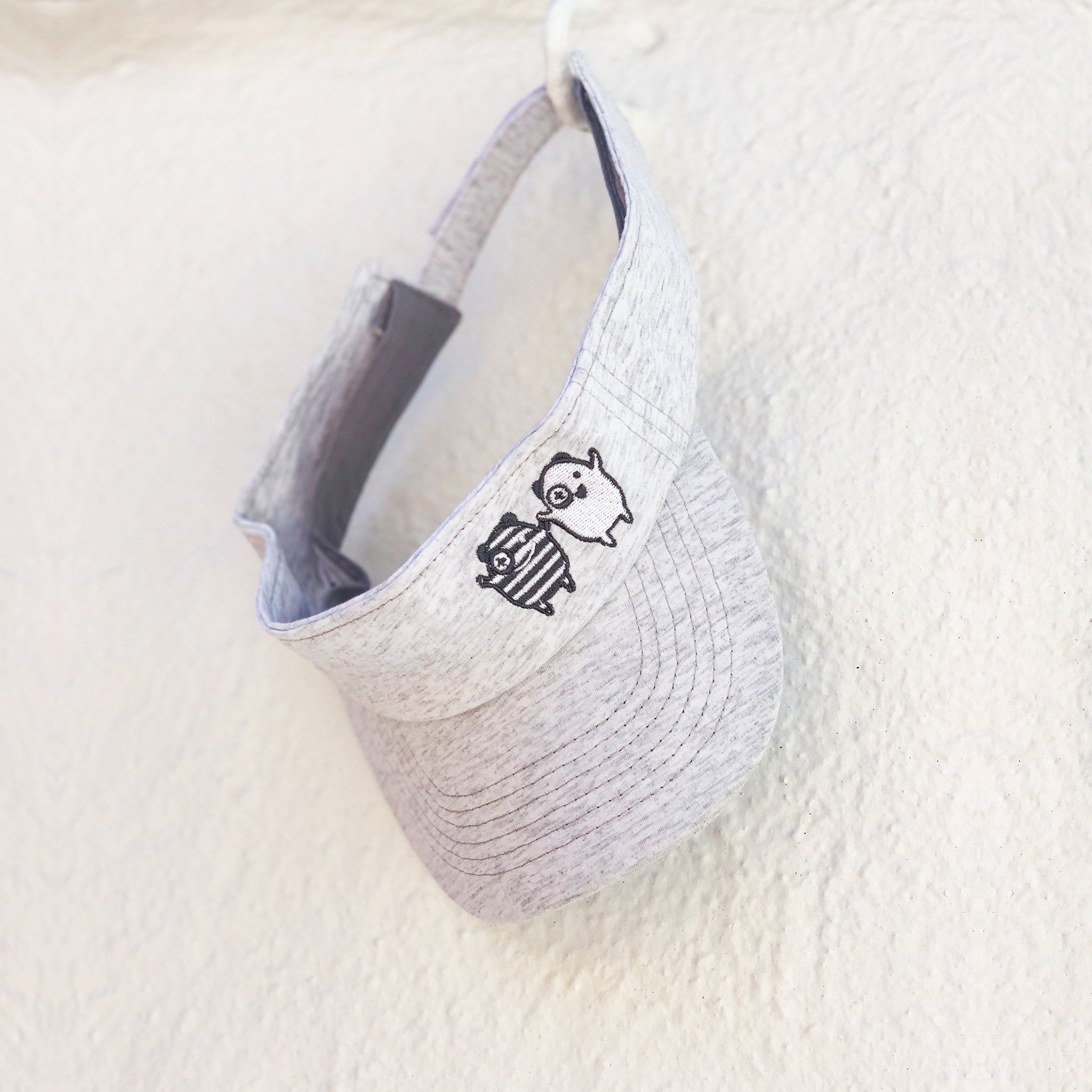 X + O Sun Visor featuring embroidered monsters and adjustable strap, perfect for sunny days.