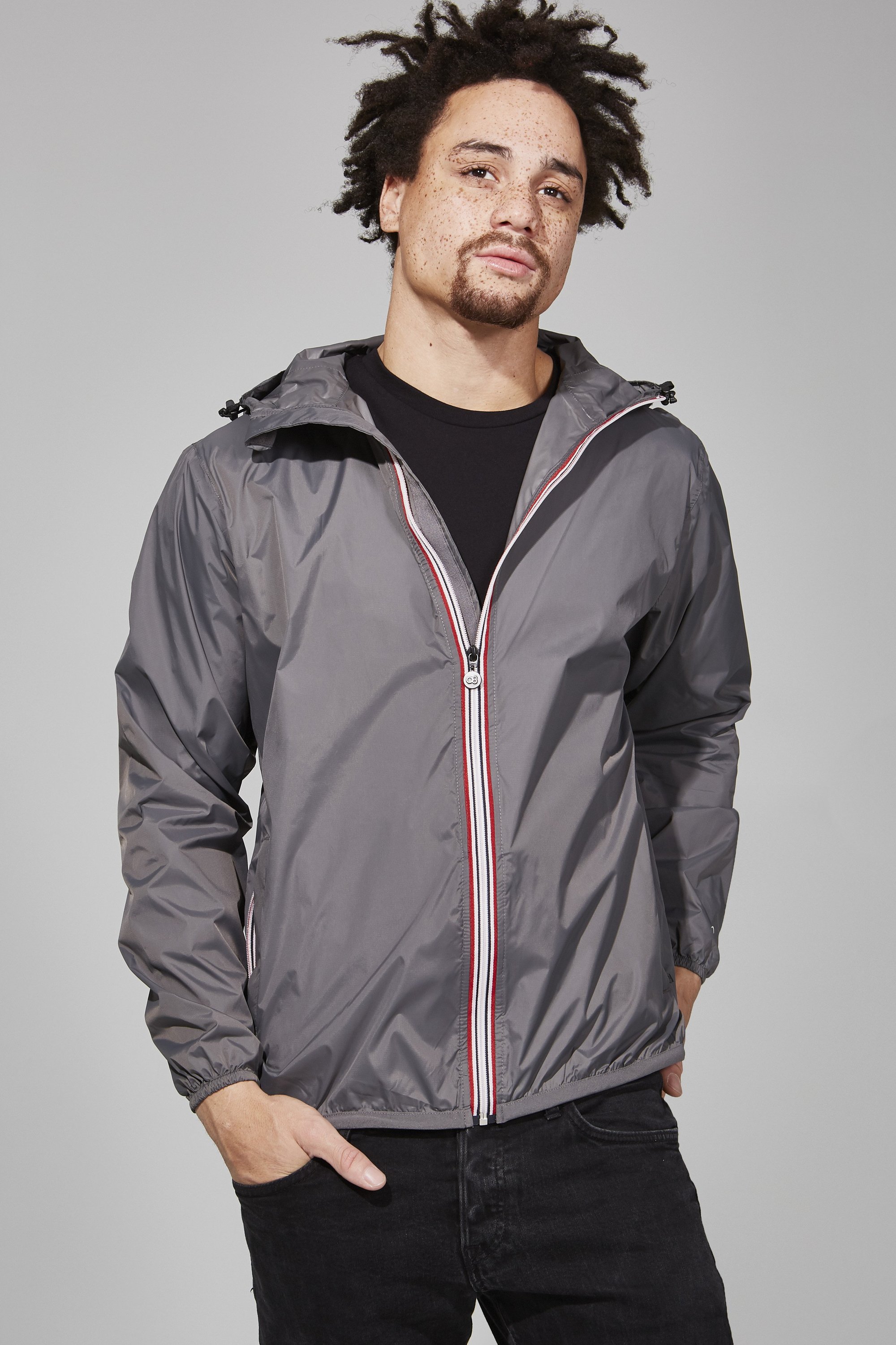 Grey full zip packable rain jacket with heat-sealed seams, folded into its side pocket, showcasing its portable design.