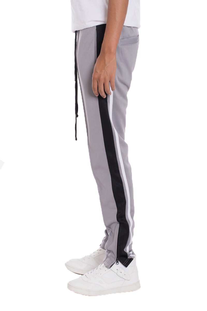 A pair of TRICOT Striped Track Pants featuring a stylish striped design, standard pockets, and a hidden ankle zipper, displayed on a model.