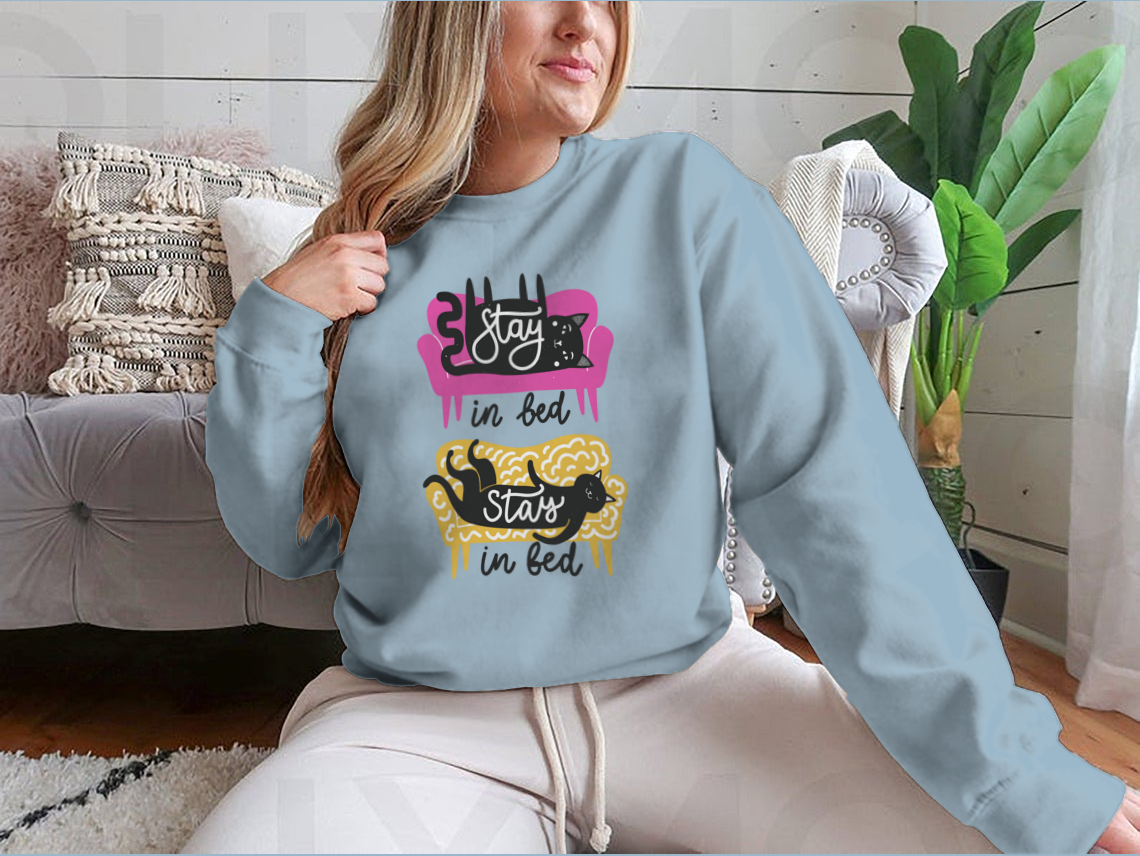 A cozy apparel featuring cats on a sofa with the text 'Stay In Bed', perfect for cat lovers.