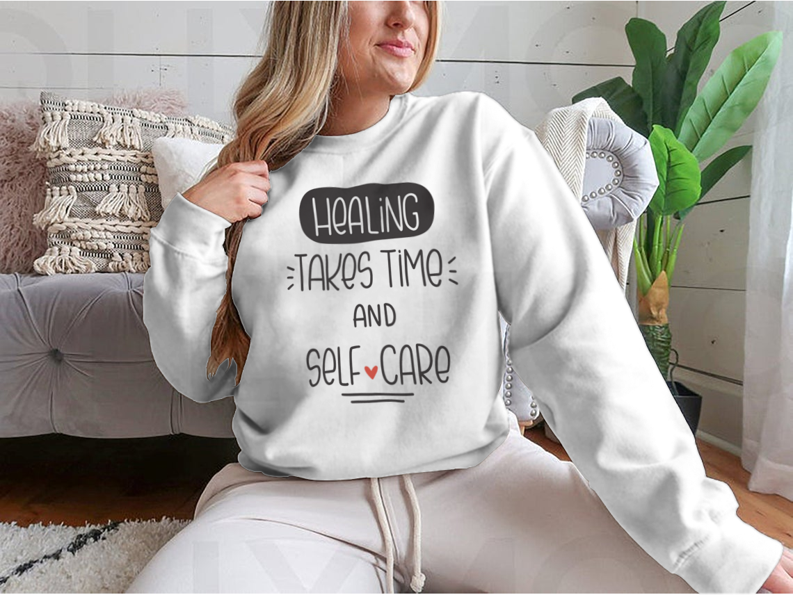 A cozy sweatshirt featuring the quote 'Healing Takes Time And Self-Care' in a stylish vector design, perfect for casual wear.