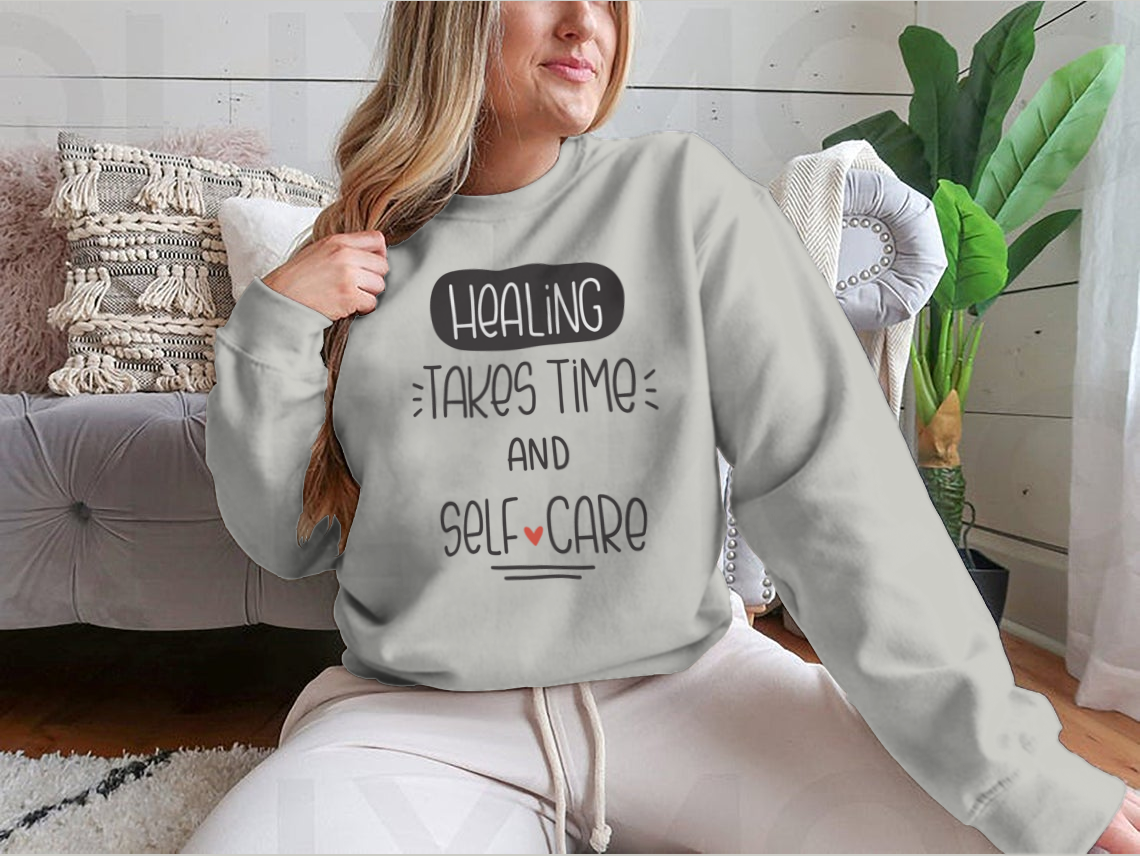A cozy sweatshirt featuring the quote 'Healing Takes Time And Self-Care' in a stylish vector design, perfect for casual wear.