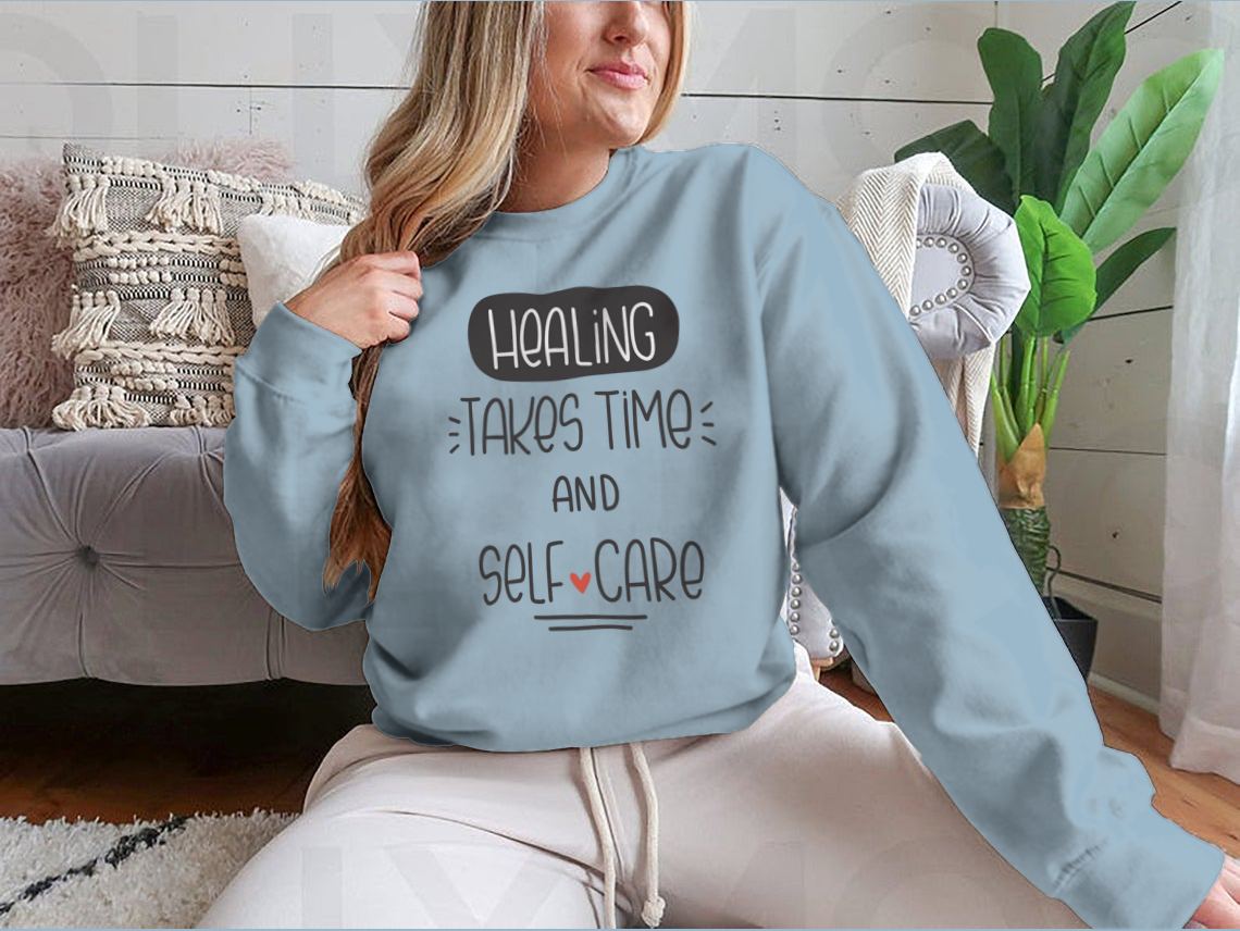 A cozy sweatshirt featuring the quote 'Healing Takes Time And Self-Care' in a stylish vector design, perfect for casual wear.