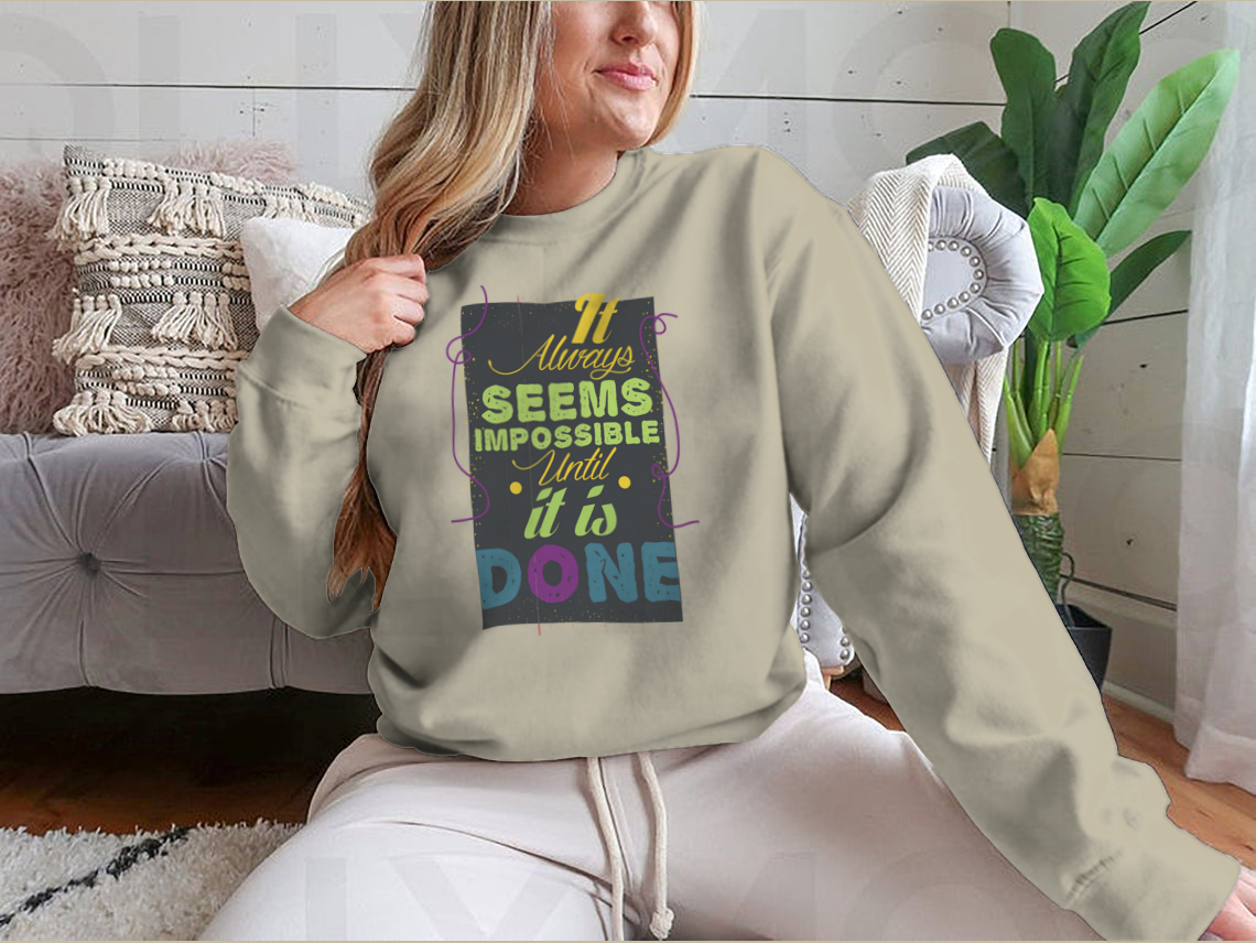 A cozy sweatshirt featuring the inspirational quote 'It Seems Impossible Until It's Done' in stylish typography, perfect for motivation.