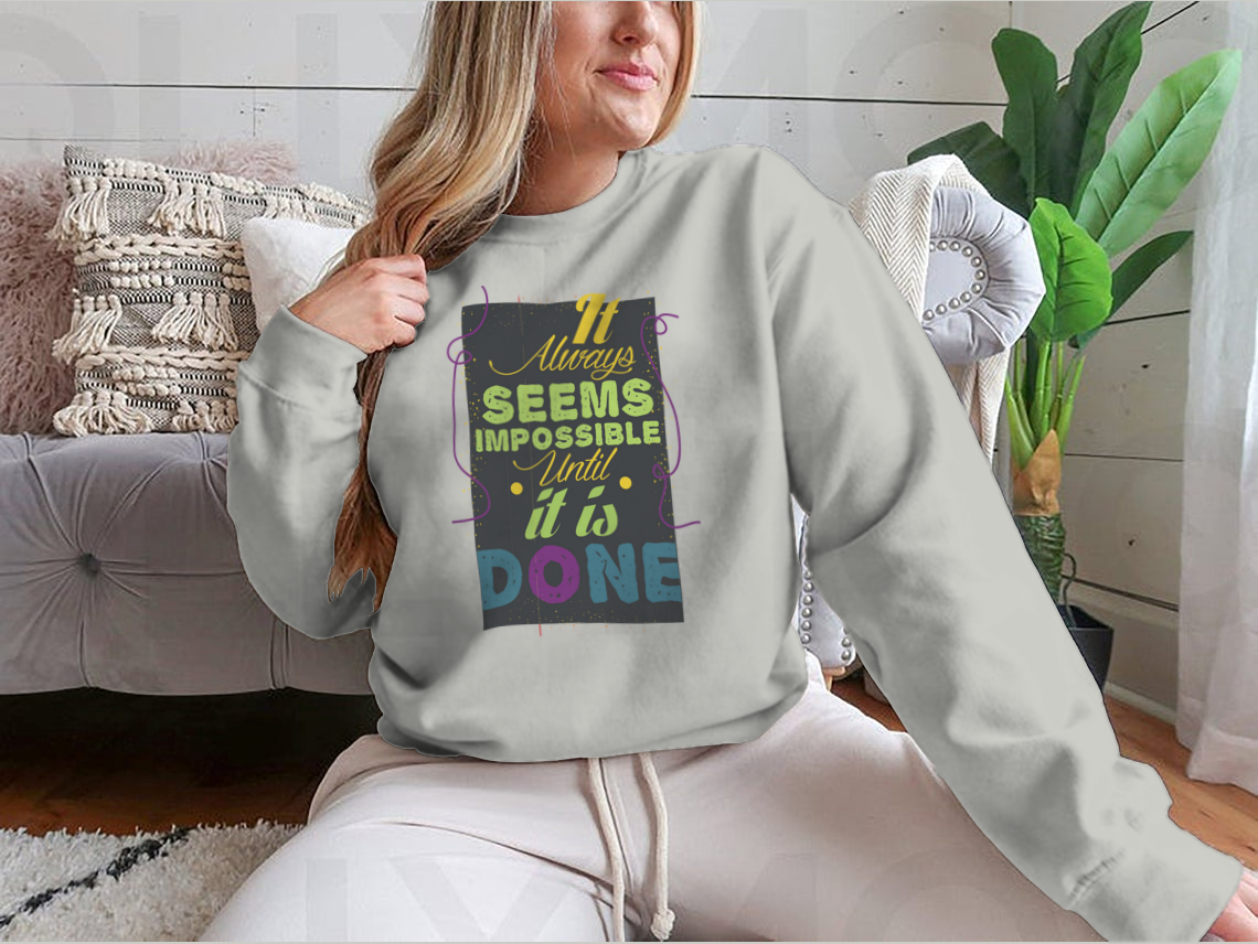 A cozy sweatshirt featuring the inspirational quote 'It Seems Impossible Until It's Done' in stylish typography, perfect for motivation.