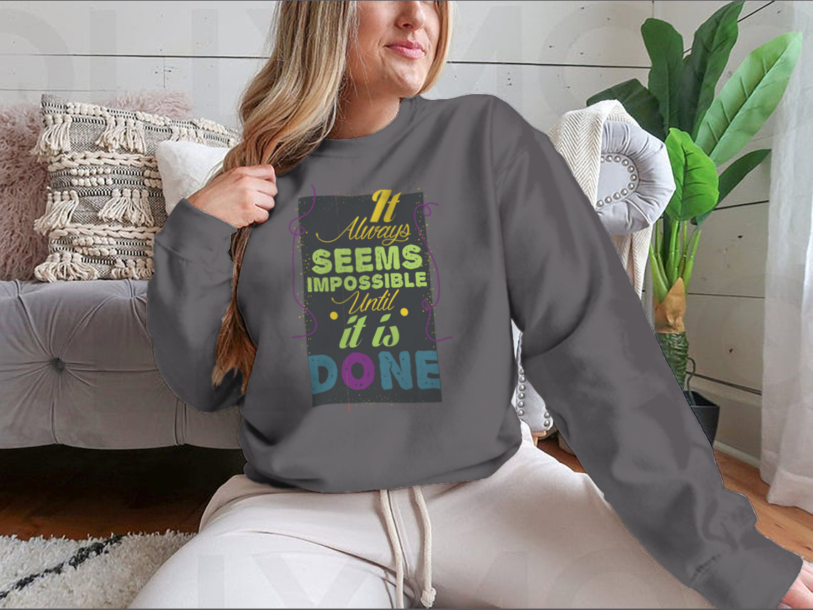 A cozy sweatshirt featuring the inspirational quote 'It Seems Impossible Until It's Done' in stylish typography, perfect for motivation.
