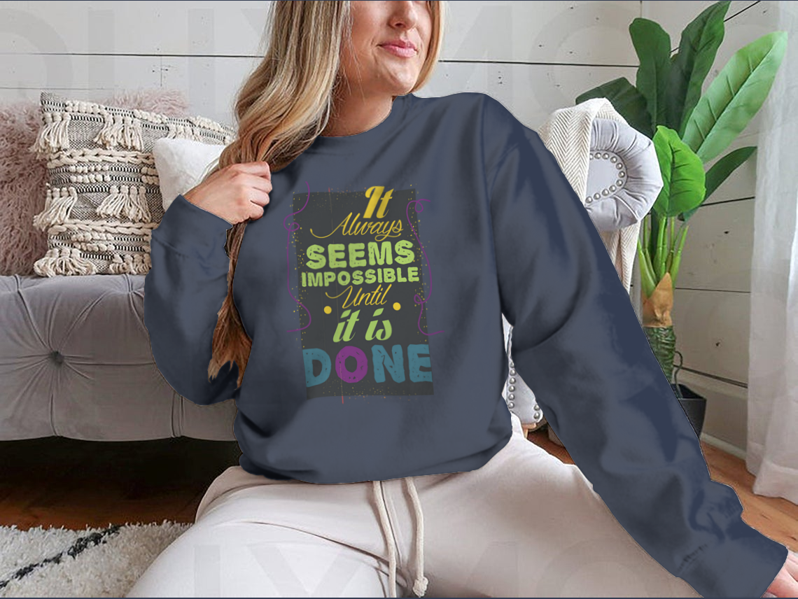 A cozy sweatshirt featuring the inspirational quote 'It Seems Impossible Until It's Done' in stylish typography, perfect for motivation.