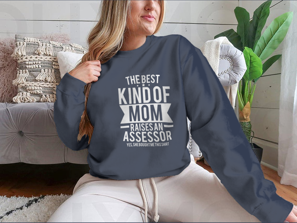 A humorous t-shirt that reads 'The Best Kind Of Mom Raises An Assessor Yes, She Bought Me This Shirt', showcasing a classic fit and soft fabric.