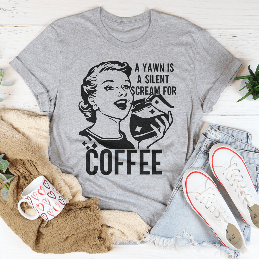 A comfortable t-shirt featuring the phrase 'A Yawn Is A Silent Scream For Coffee' printed on it, made from soft ring-spun cotton.
