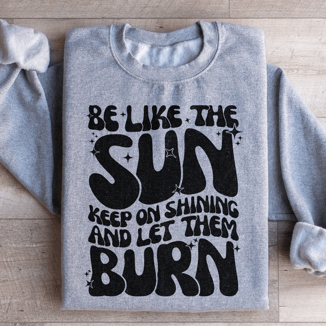 A cozy hoodie featuring the phrase 'Be Like The Sun Keep On Shining And Let Them Burn', designed by top artists, showcasing vibrant colors and a stylish fit.