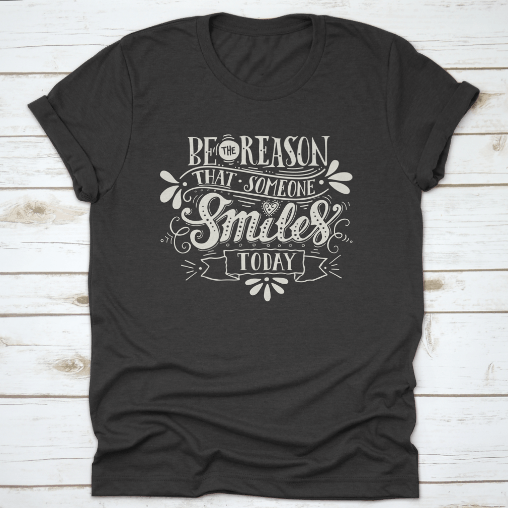 A motivational shirt with the phrase 'Be The Reason That Someone Smiles Today' printed on it, showcasing a classic fit and made from soft cotton fabric.