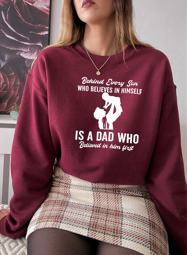 A cozy sweatshirt featuring the phrase 'Behind Every Son Who Believes In Himself', designed by top artists, showcasing a stylish and comfortable fit.