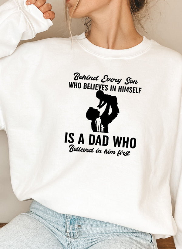 A cozy sweatshirt featuring the phrase 'Behind Every Son Who Believes In Himself', designed by top artists, showcasing a stylish and comfortable fit.