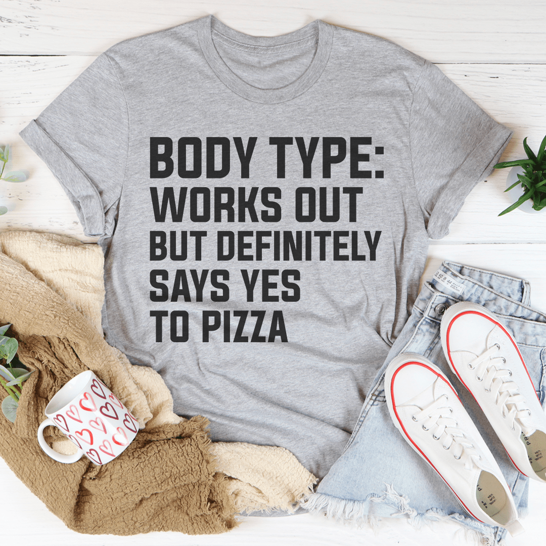 A comfortable and stylish t-shirt featuring the phrase 'Body Type Works Out But Definitely Says Yes To Pizza' in a playful design.