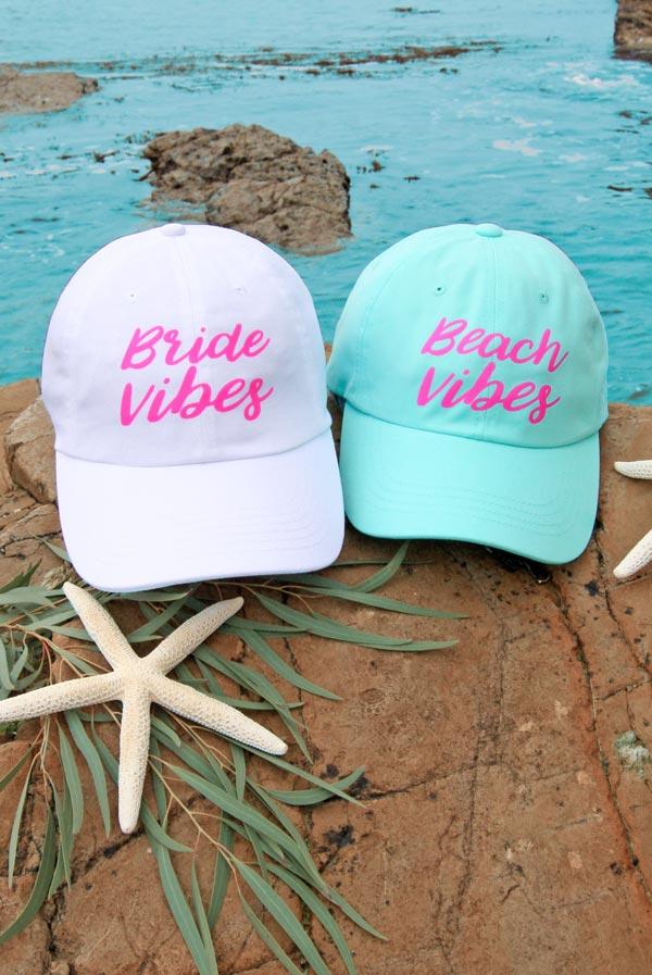 Two stylish dad hats for bachelorette parties, one white with 'Bride Vibes' and one mint with 'Beach Vibes', perfect for beach and poolside fun.
