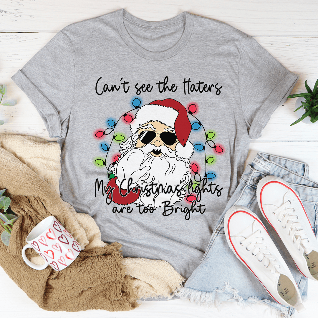 A festive Christmas tee featuring the phrase 'Can't See The Haters My Christmas Lights Are Too Bright' printed in vibrant colors on a soft cotton fabric.