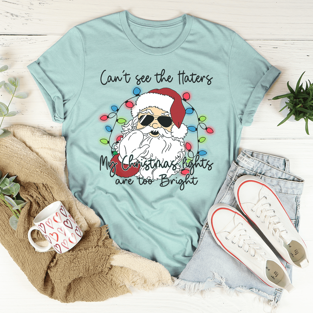 A festive Christmas tee featuring the phrase 'Can't See The Haters My Christmas Lights Are Too Bright' printed in vibrant colors on a soft cotton fabric.