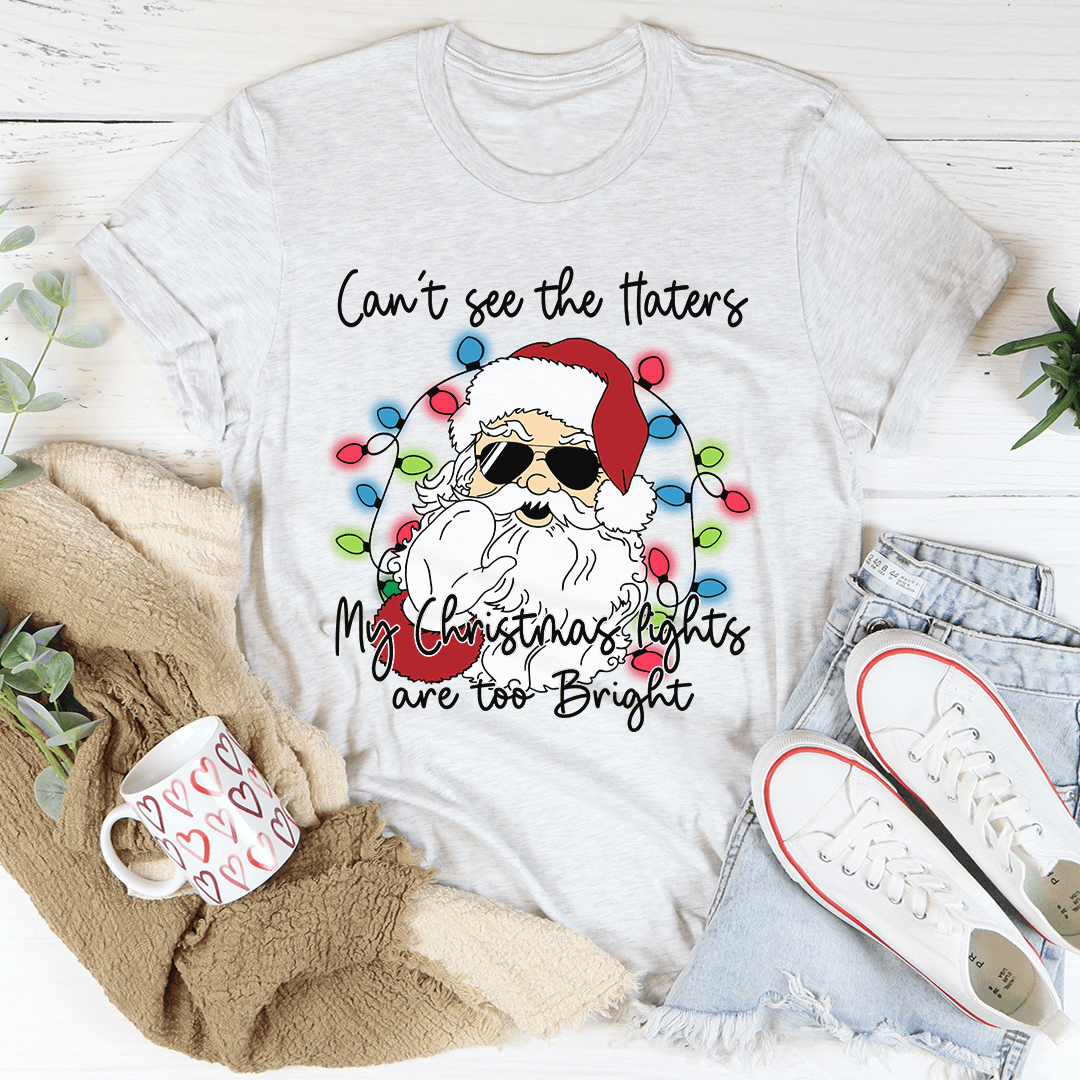 A festive Christmas tee featuring the phrase 'Can't See The Haters My Christmas Lights Are Too Bright' printed in vibrant colors on a soft cotton fabric.