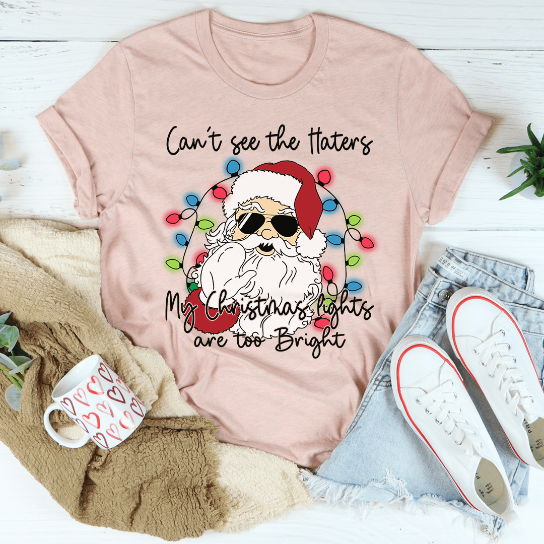 A festive Christmas tee featuring the phrase 'Can't See The Haters My Christmas Lights Are Too Bright' printed in vibrant colors on a soft cotton fabric.