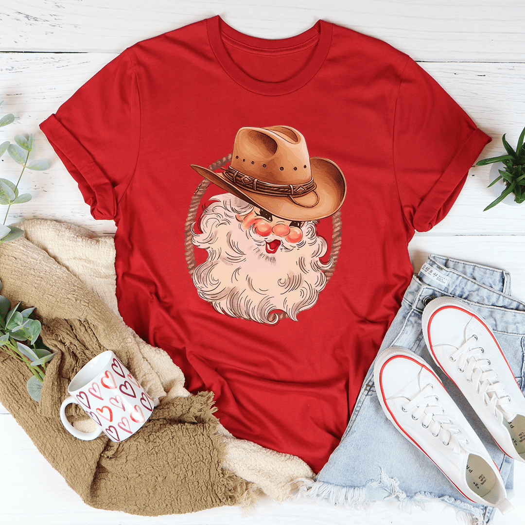 A festive Cowboy Santa Tee featuring a vibrant digital print of Santa in cowboy attire, made from 100% soft cotton.