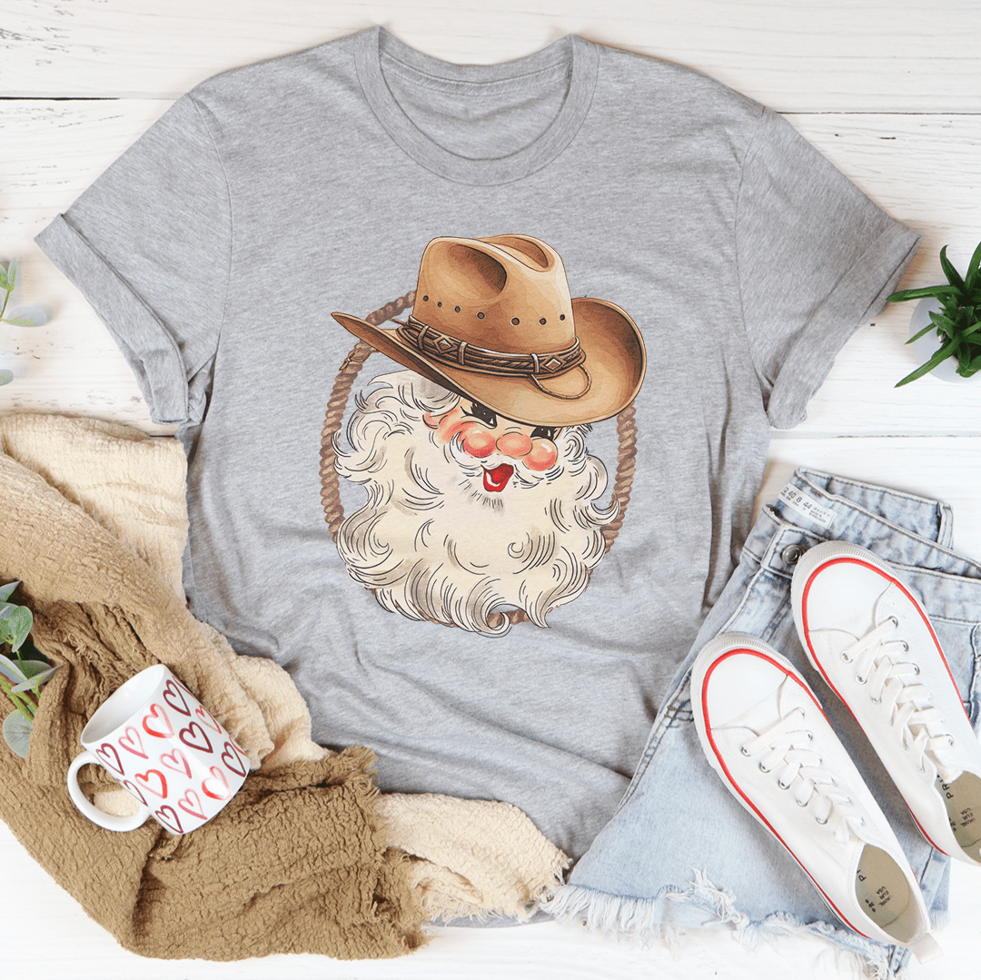 A festive Cowboy Santa Tee featuring a vibrant digital print of Santa in cowboy attire, made from 100% soft cotton.