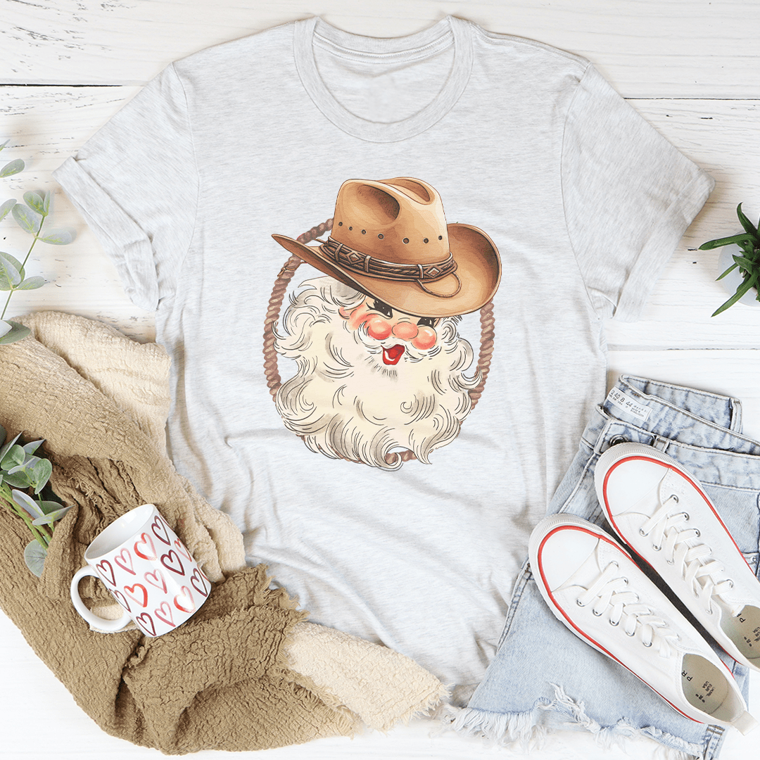 A festive Cowboy Santa Tee featuring a vibrant digital print of Santa in cowboy attire, made from 100% soft cotton.