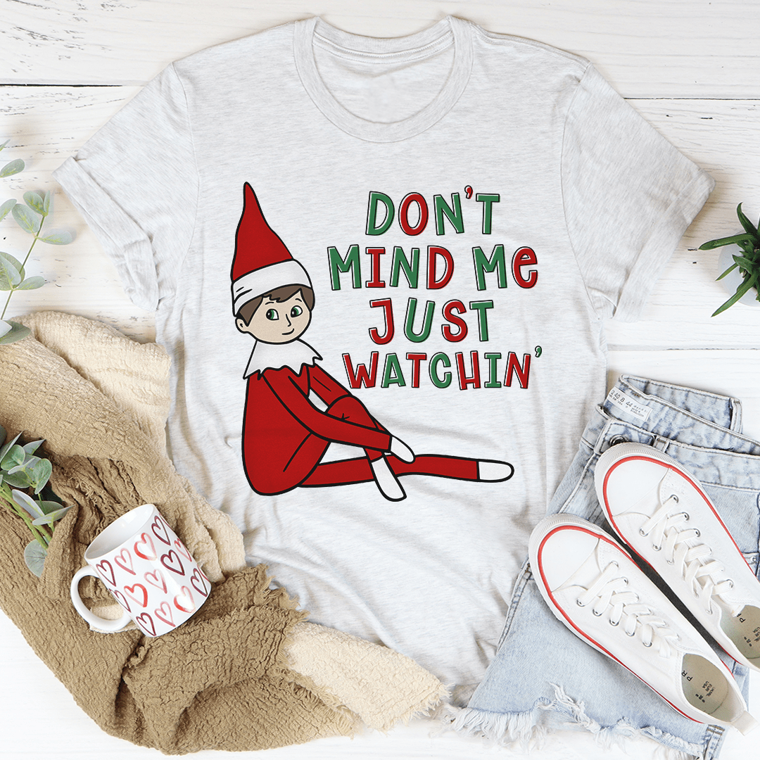 A festive Christmas-themed tee featuring the phrase 'Don't Mind Me Just Watchin' printed in vibrant colors on a soft cotton fabric.