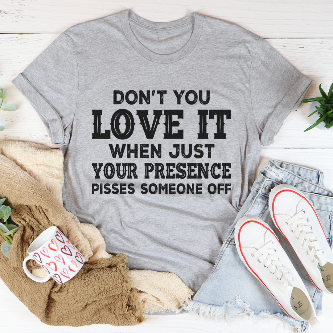 A black t-shirt featuring the phrase 'Don't You Love It When Just Your Presence Pisses Someone Off' in bold white lettering, showcasing its comfortable fit and durable fabric.