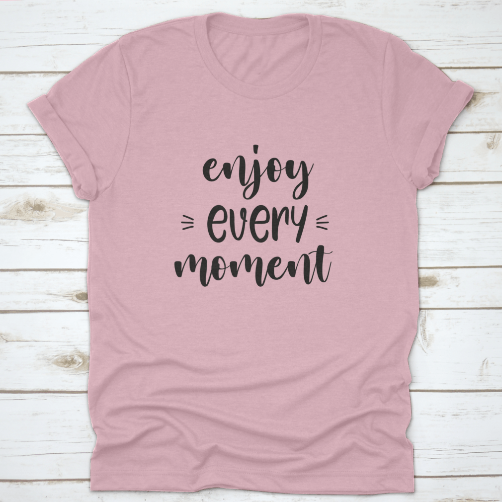 A stylish t-shirt featuring the phrase 'Enjoy Every Moment' in brush lettering design, made from soft cotton fabric.