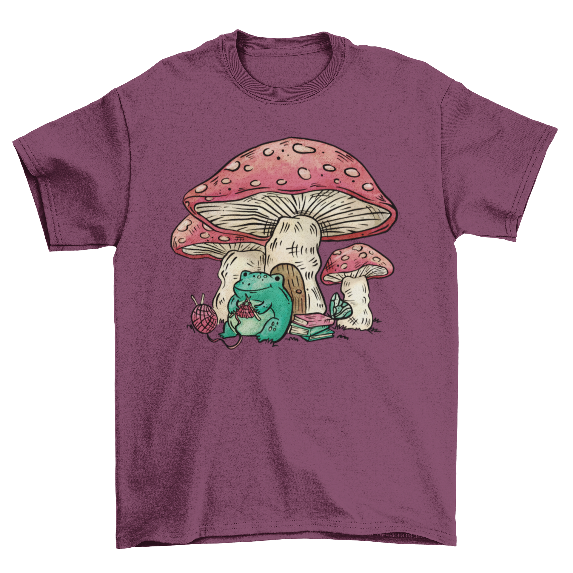 A whimsical t-shirt featuring a cheerful frog knitting next to a colorful mushroom house.
