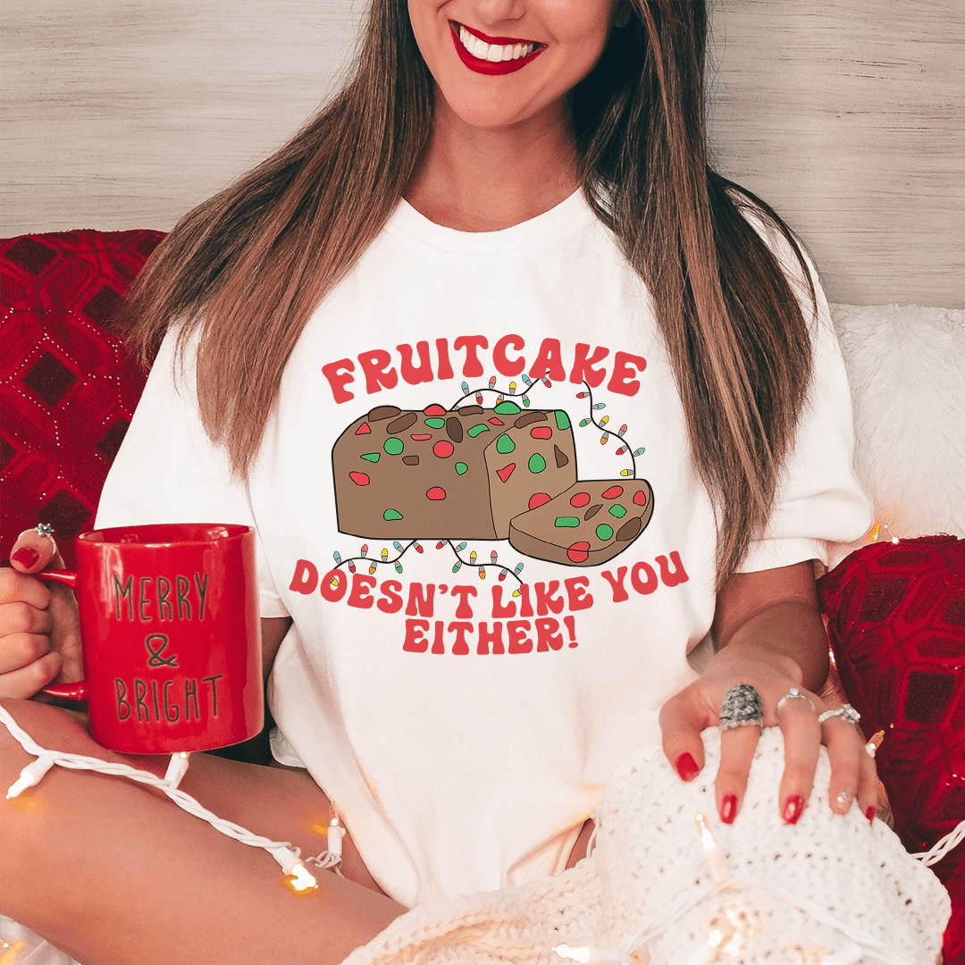 A festive tee featuring the phrase 'Fruitcake Doesn't Like You Either', printed on soft cotton fabric, perfect for holiday celebrations.