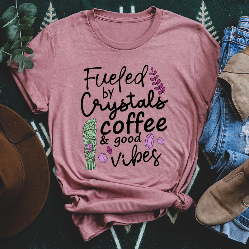 A stylish t-shirt featuring the phrase 'Fueled By Crystals Coffee & Good Vibes' printed in vibrant colors on soft cotton fabric.