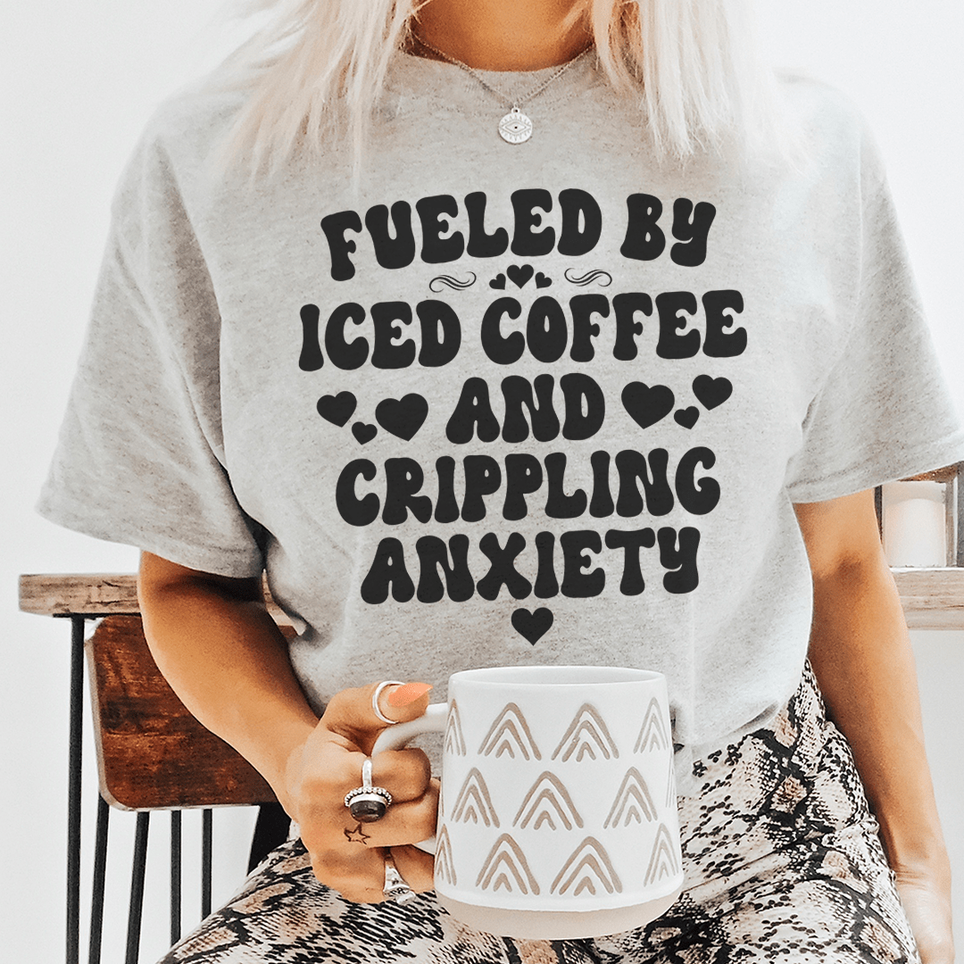 A humorous t-shirt featuring the phrase 'Fueled By Iced Coffee And Crippling Anxiety', made from soft cotton with double stitching.