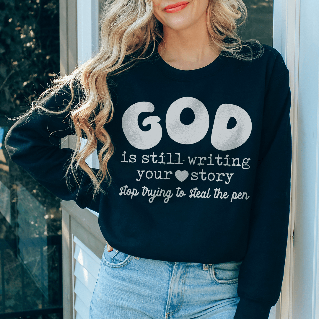 A cozy hoodie featuring the phrase 'God Is Still Writing Your Story', designed by top artists, showcasing a unique artistic design.