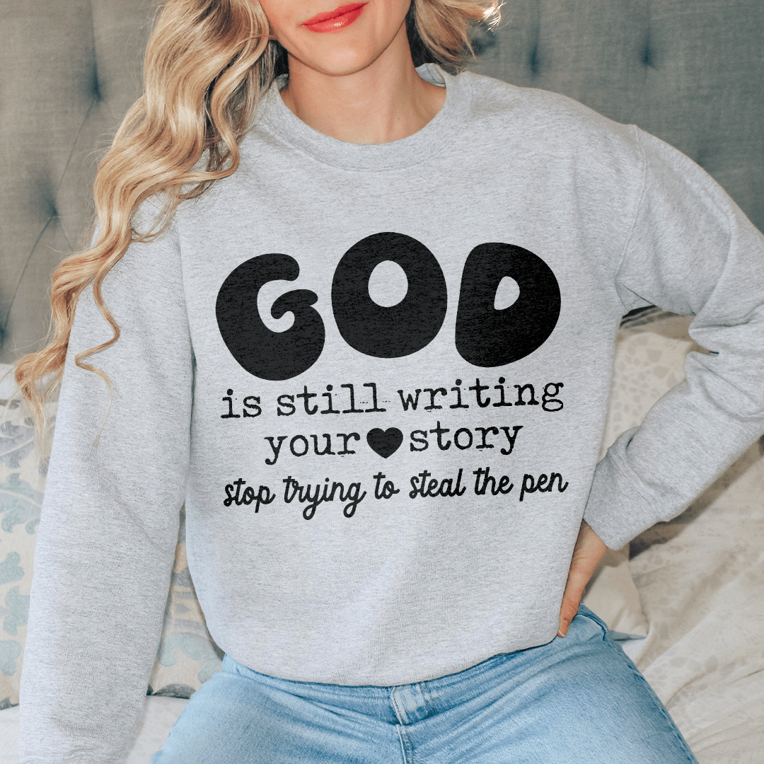 A cozy hoodie featuring the phrase 'God Is Still Writing Your Story', designed by top artists, showcasing a unique artistic design.