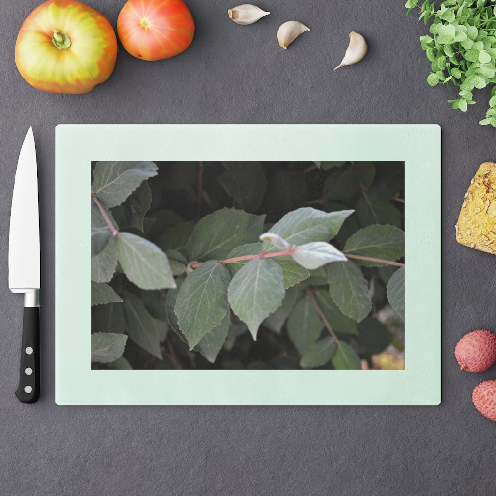 A stylish Green Leaves Cutting Board made of tempered glass, featuring a vibrant green leaves design and four rubber dots for stability.