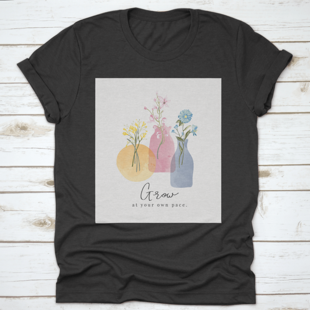 A colorful t-shirt featuring the slogan 'Grow At Your Own Pace' with a watercolor flower vase design, showcasing vibrant floral patterns.