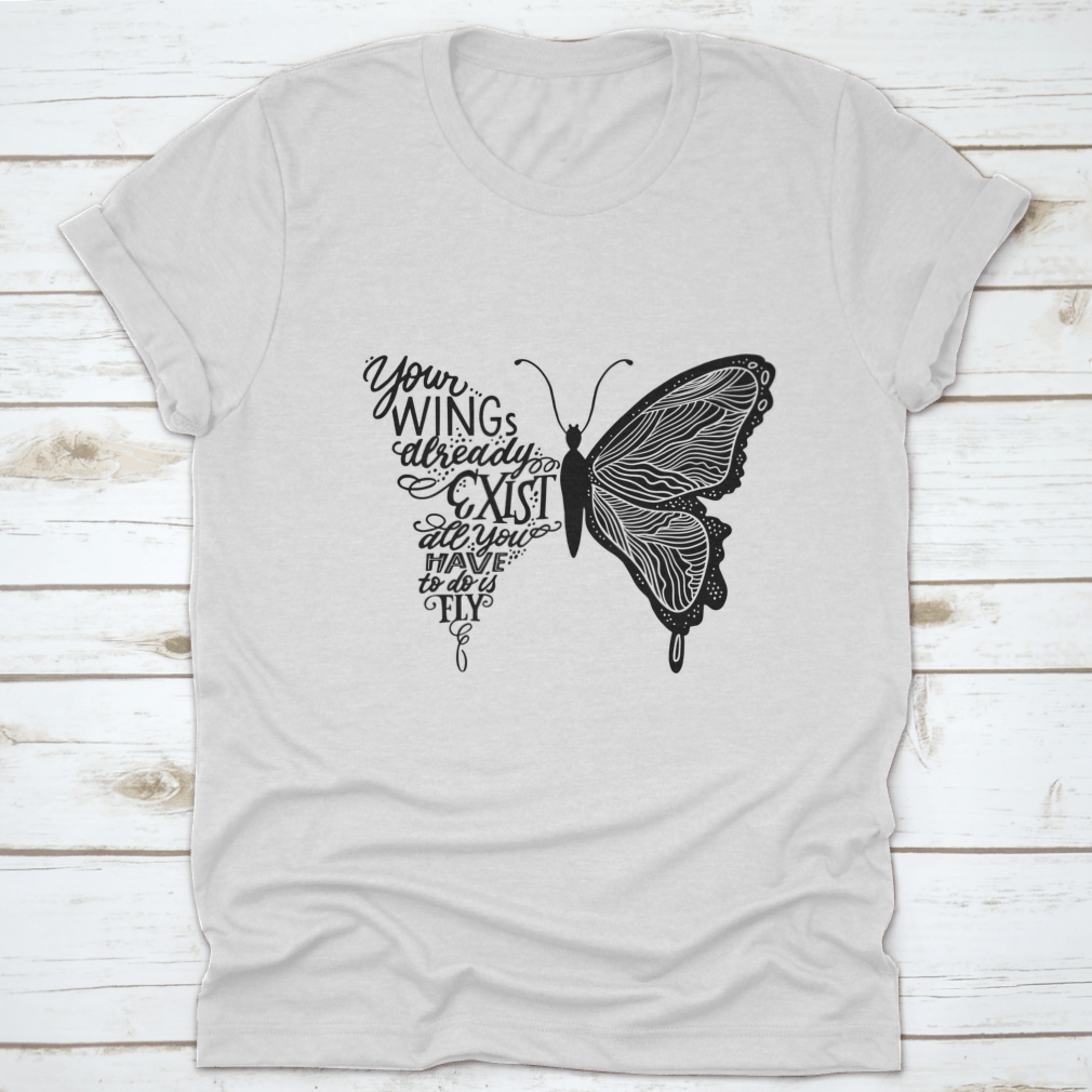 A stylish t-shirt featuring hand lettering in a butterfly silhouette design, showcasing the phrase 'Your Wings Already Exists All' on a soft fabric.